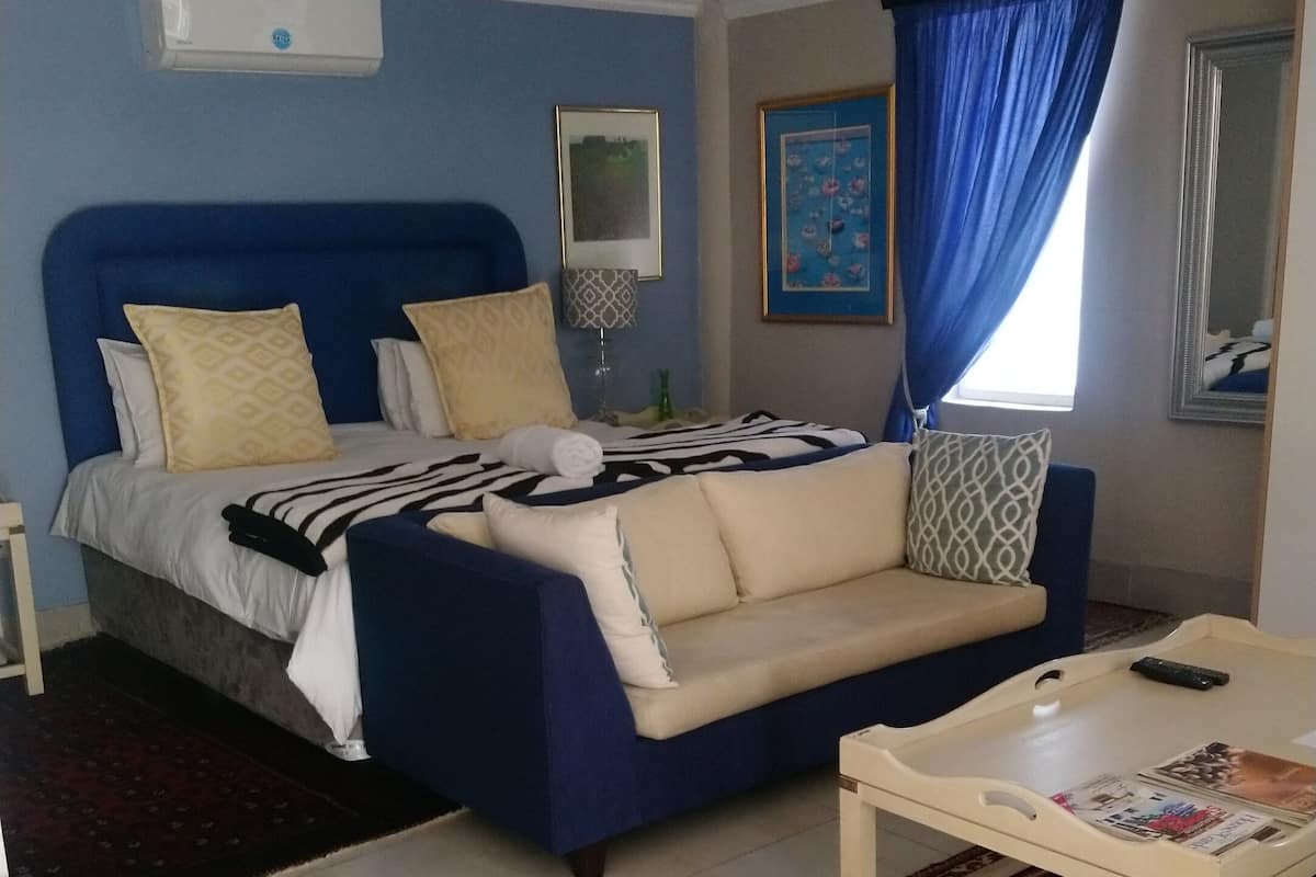 A bedroom with a bed, a sofa, a coffee table, a rug, and a window with curtains.