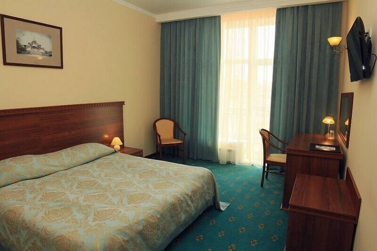 A hotel room with a large bed, two chairs, a desk, and a lamp.