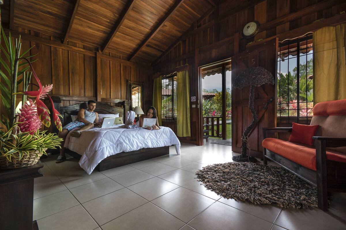 A wooden room with a bed, a red sofa, and a large potted plant.