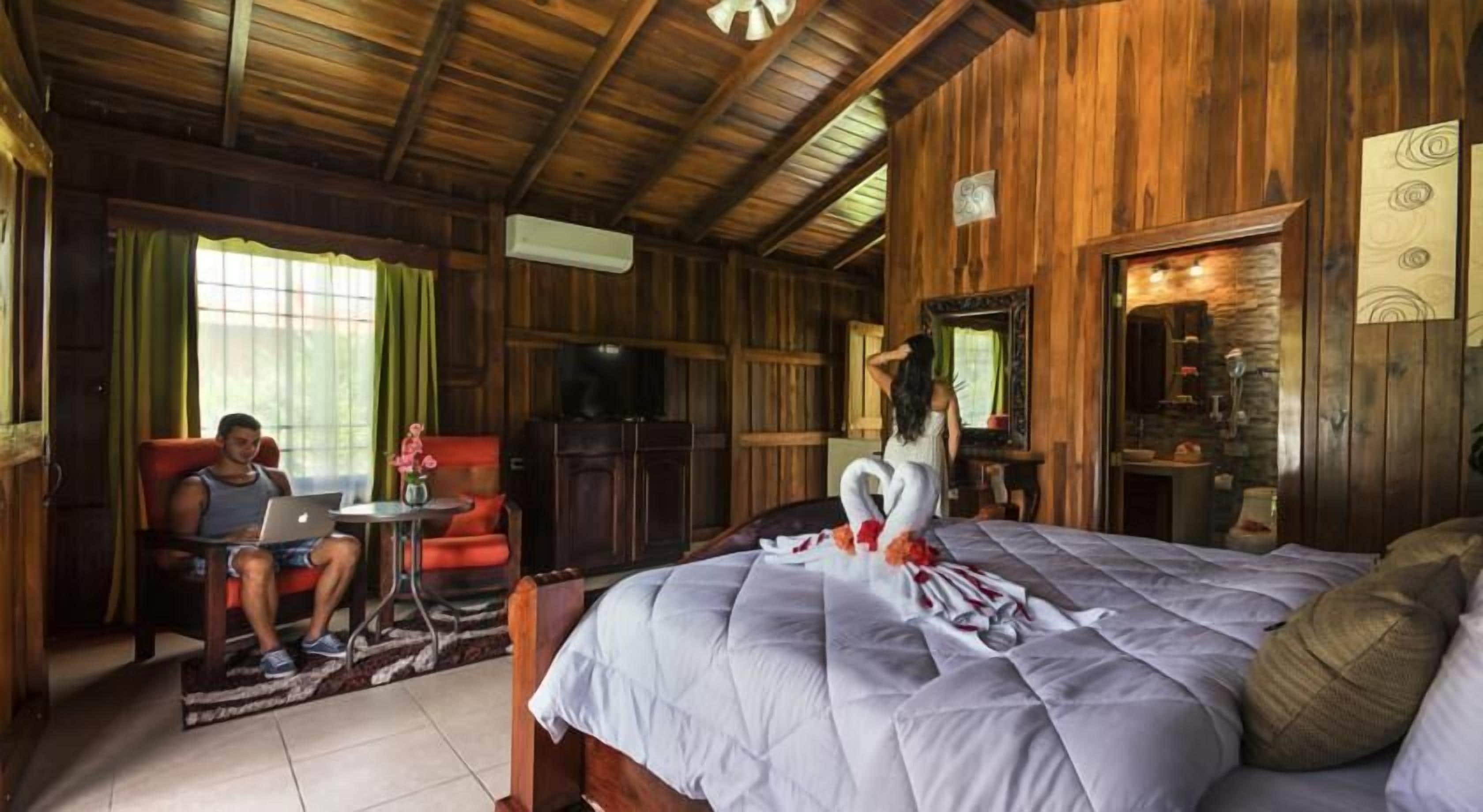 A wooden cabin room with a bed, a desk, and a chair.