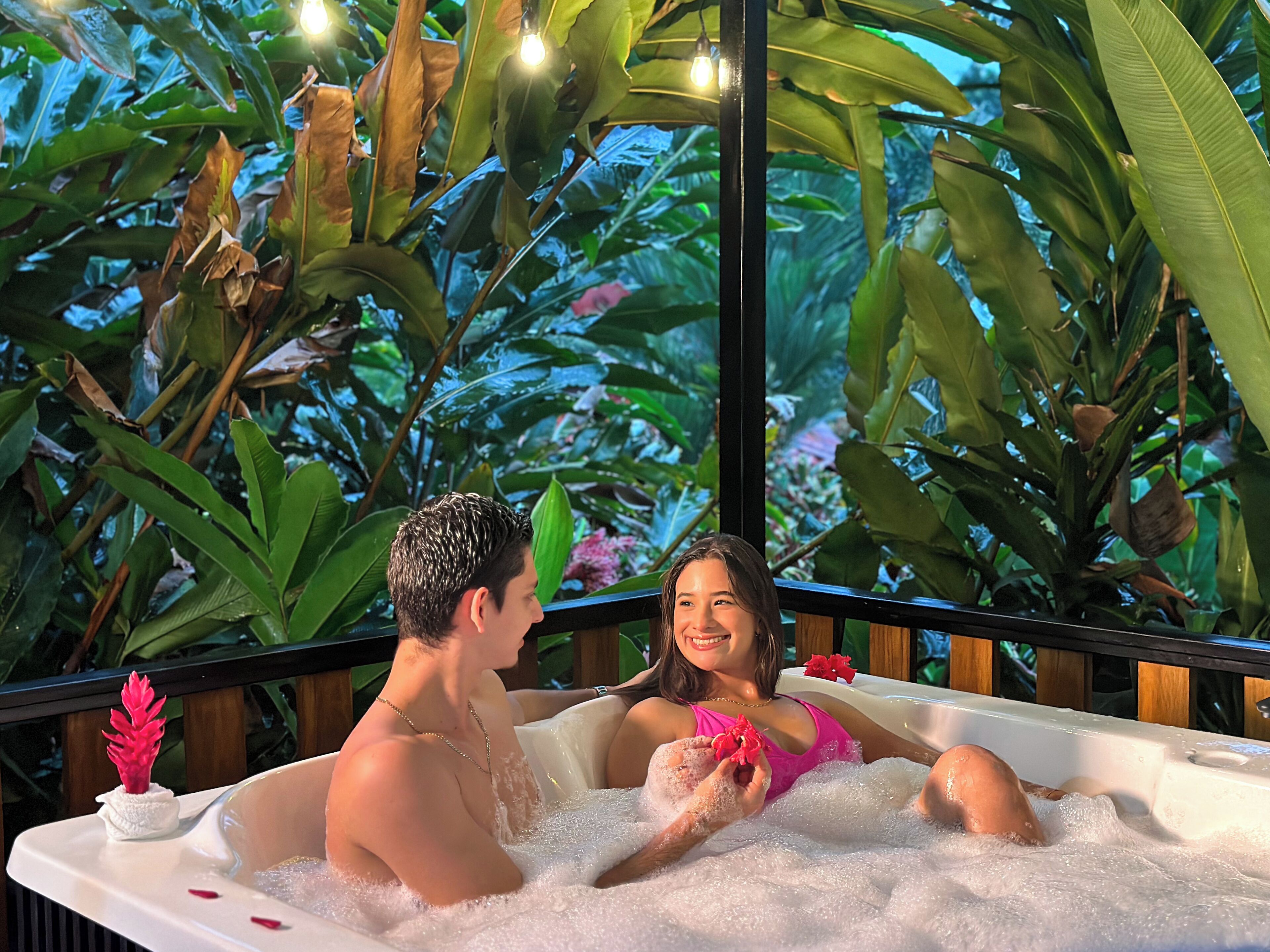 Una pareja relajándose en un jacuzzi rodeado de exuberante follaje tropical.