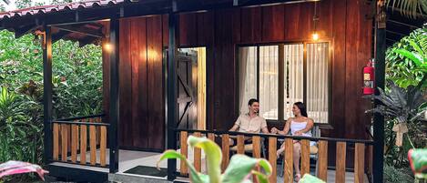 A wooden cabin with a porch, a fire extinguisher, and a view of the surrounding greenery.