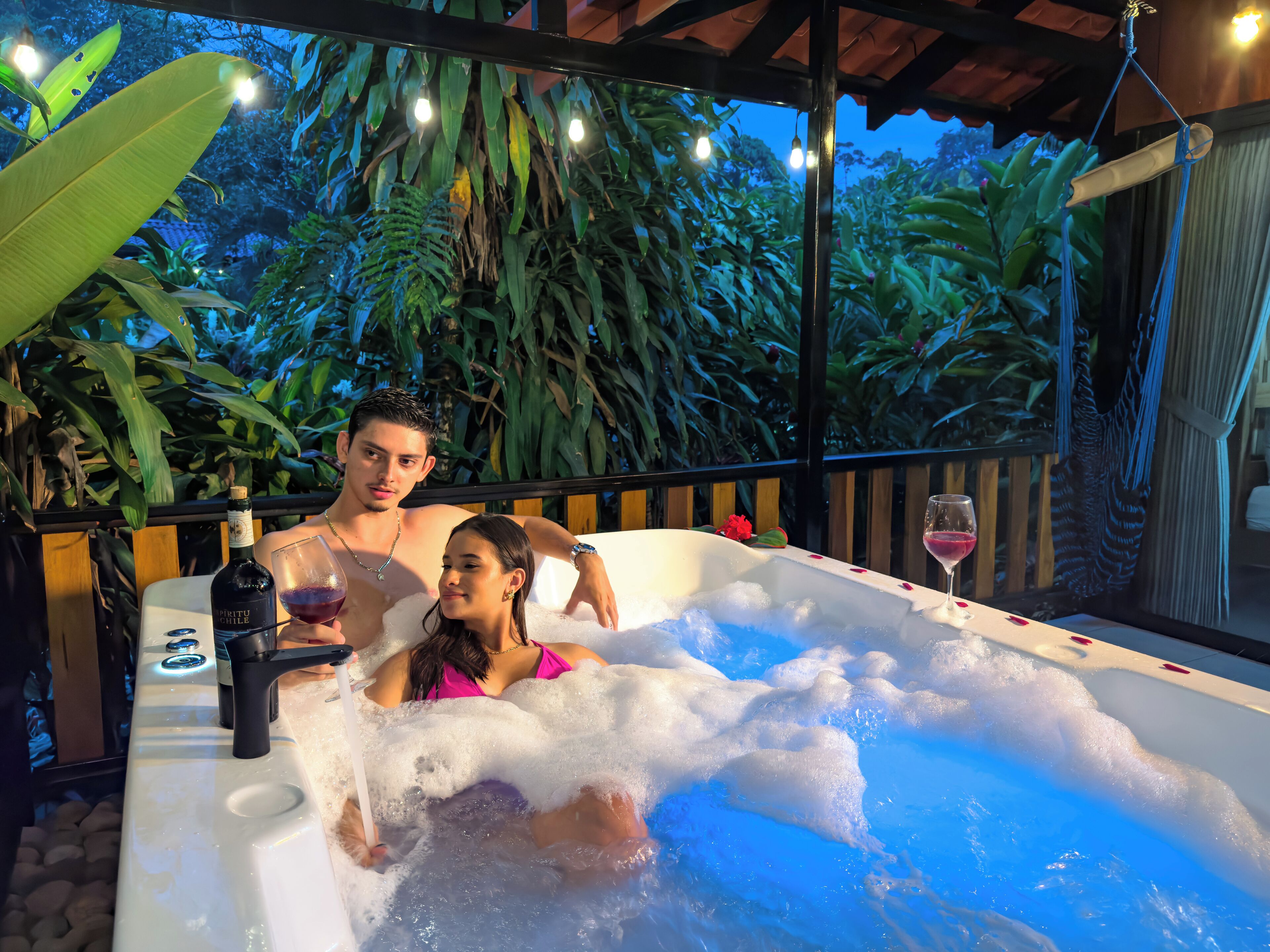 A couple in a hot tub with a bottle of wine and a glass of wine.