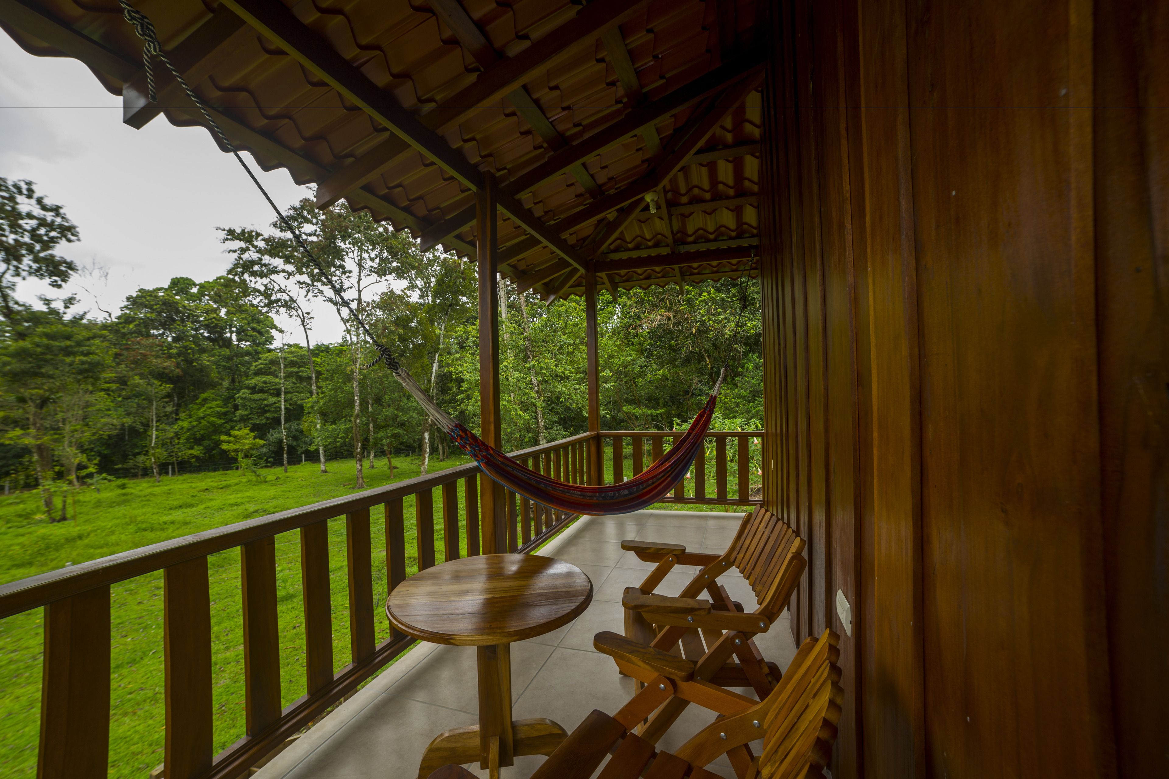 A wooden deck with a hammock, wooden chairs, and a table.