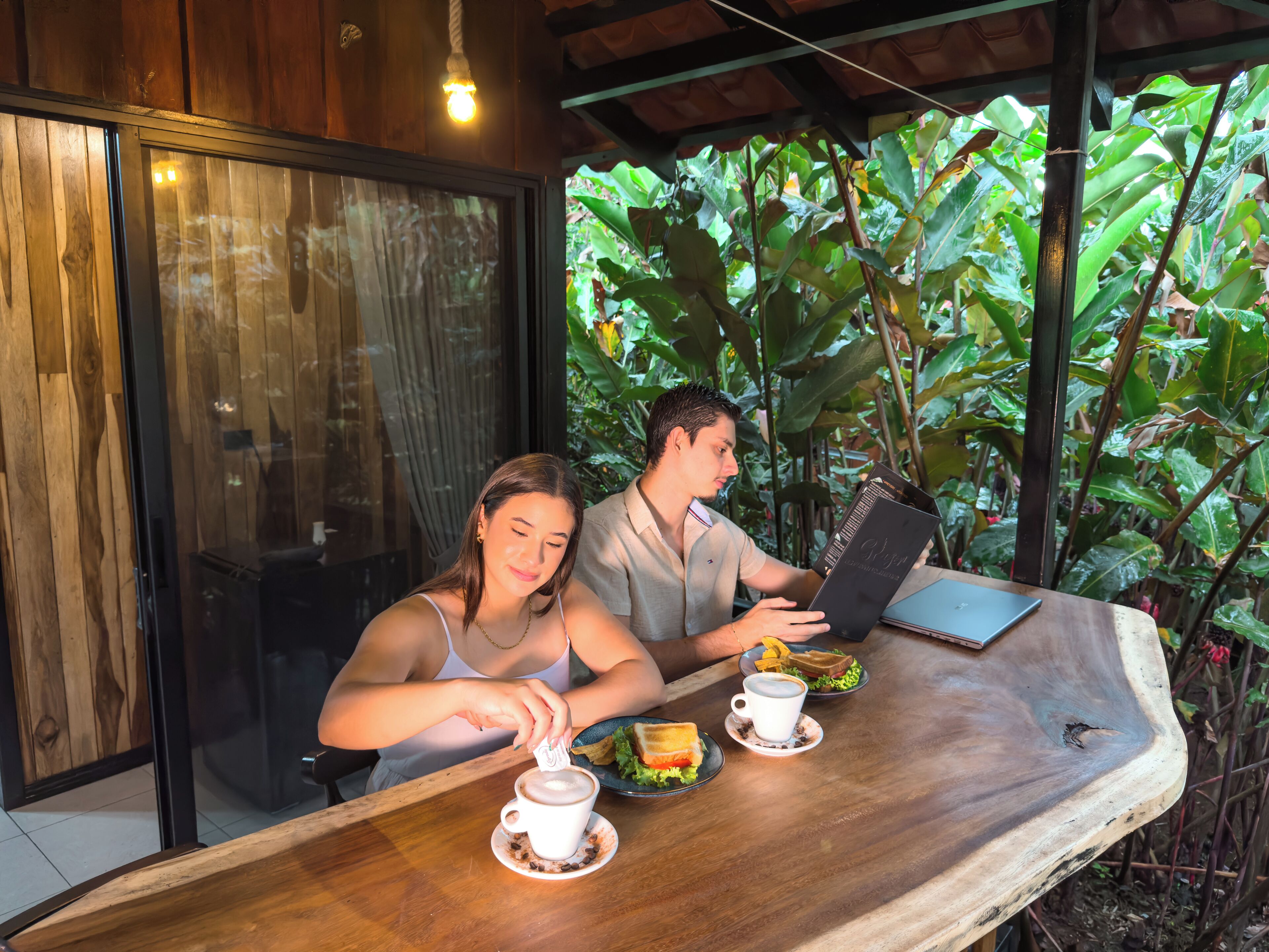 A wooden table with a cup of coffee, a sandwich, and a menu.