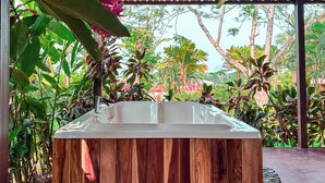 Un bain à remous en bois, entouré de rochers et de plantes tropicales, installé sous un toit recouvert de tuiles.