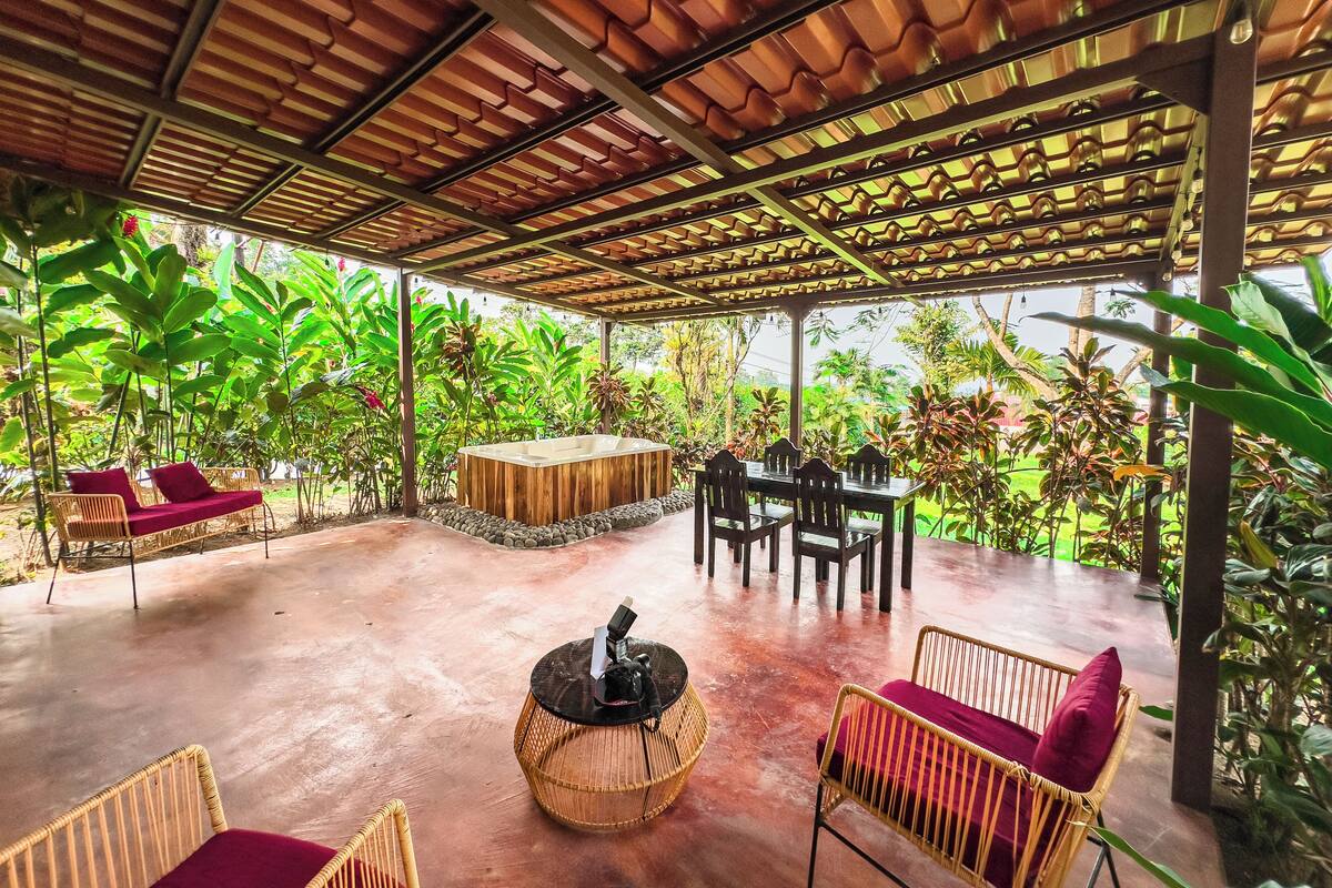 A covered outdoor area with a wooden table, chairs, and a hot tub.