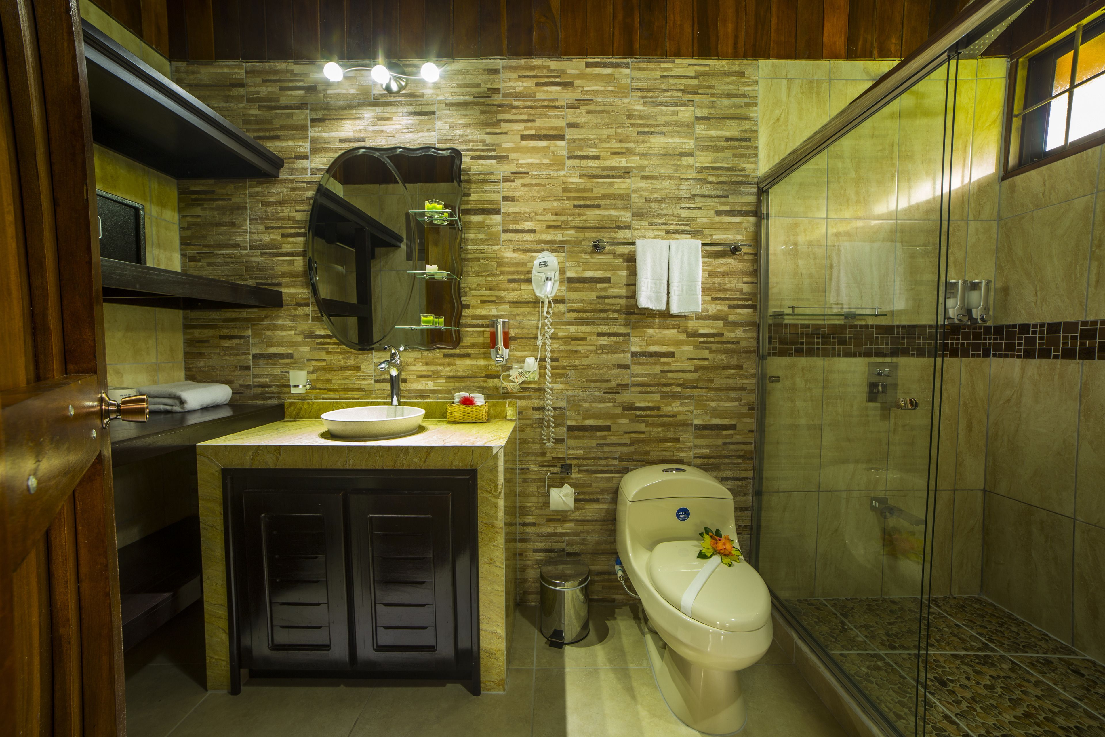 A bathroom with a stone backsplash, a sink, a toilet, and a glass-enclosed shower.