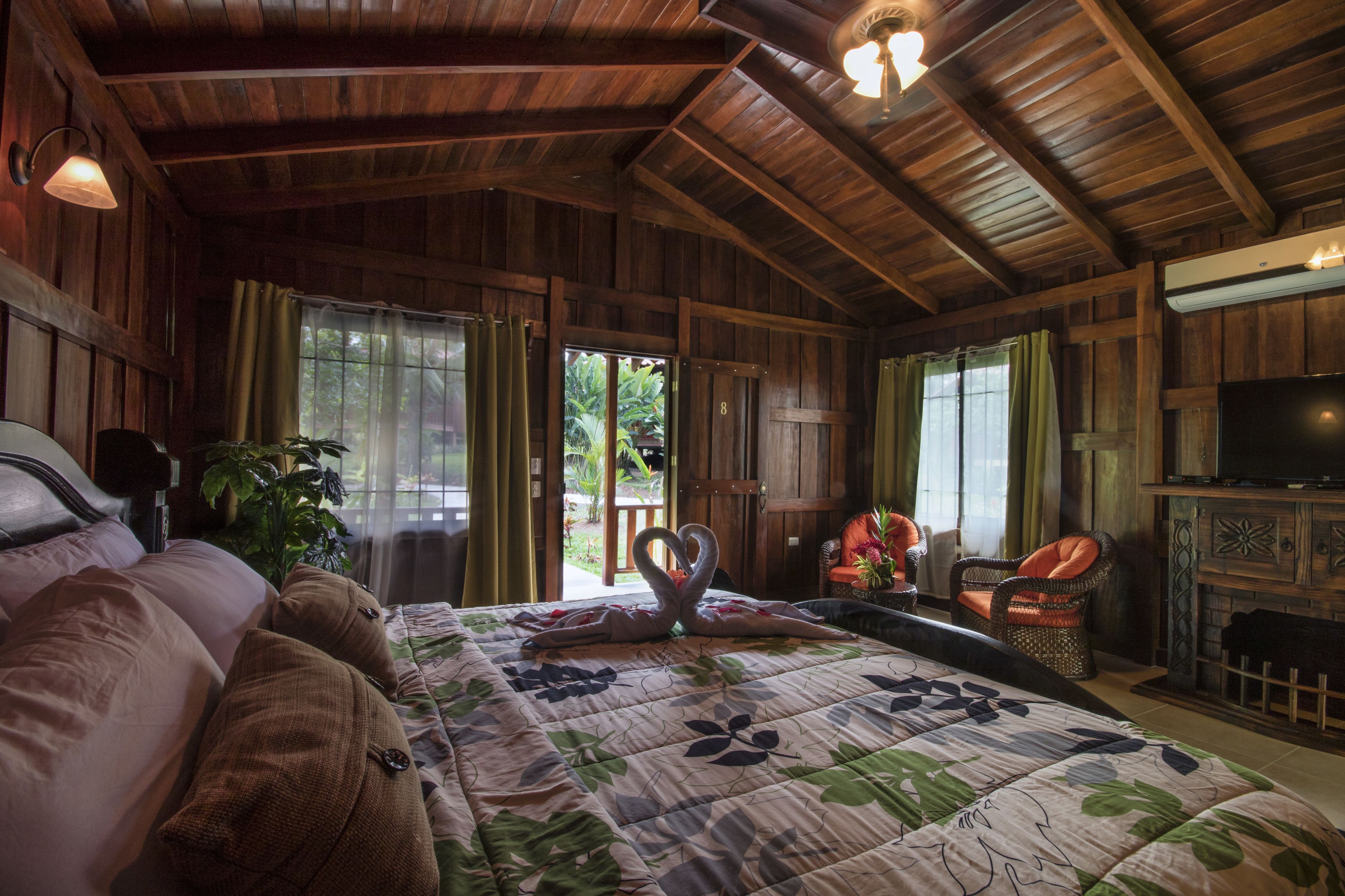 A wooden cabin-style room with a bed, a television, a fireplace, and a balcony with curtains.