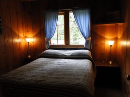 A wooden room with a bed, two bedside lamps, and a window with curtains.