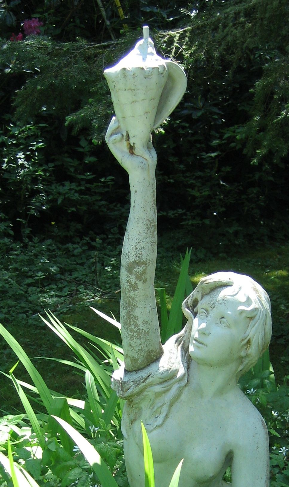 A statue of a figure holding a cup, surrounded by greenery.