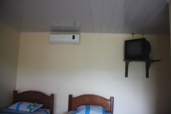 A room with two wooden beds, a ceiling-mounted air conditioner, and a television on a stand.