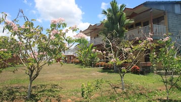 A hotel with multiple balconies, a grassy lawn, and flowering trees.