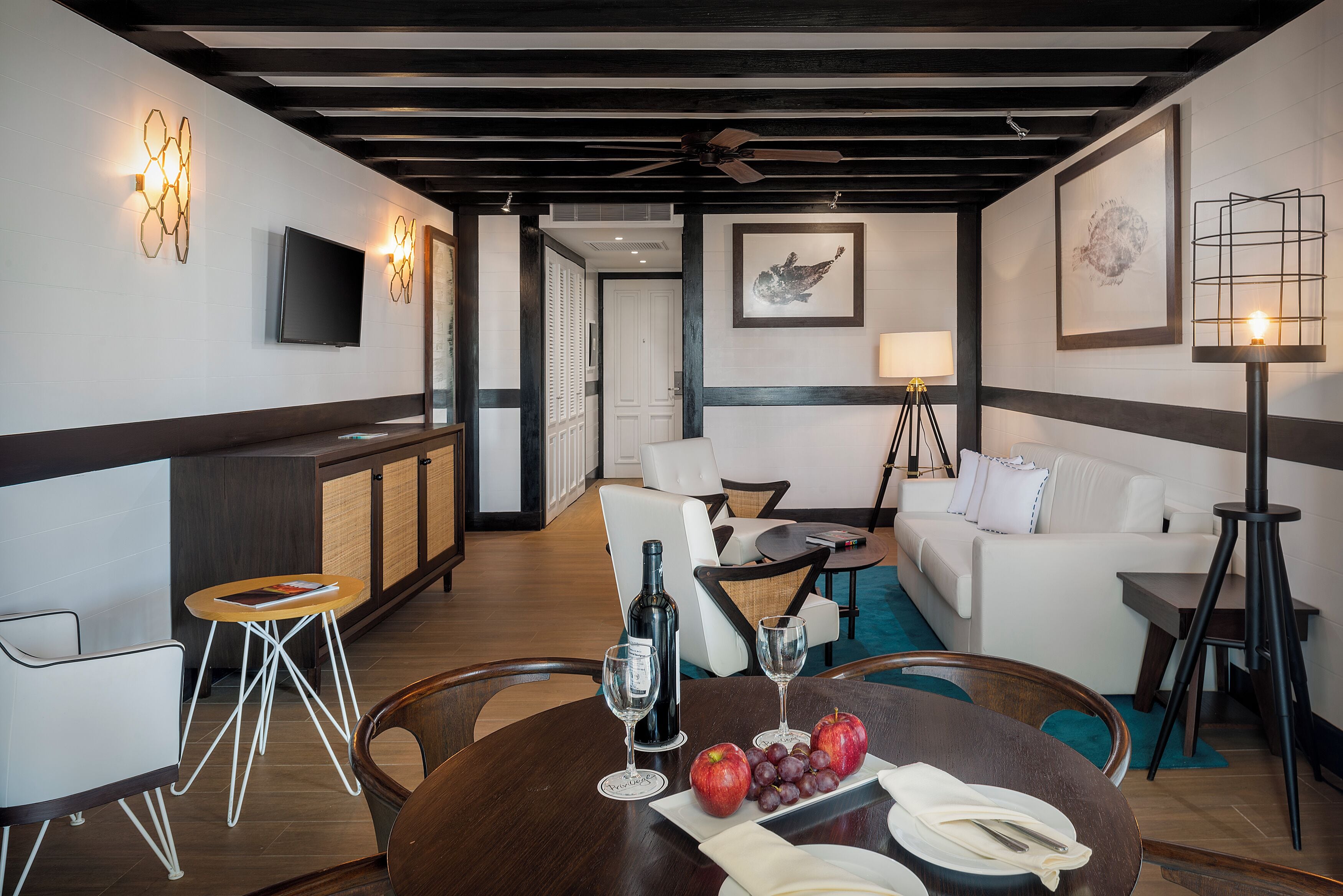 Quarto de hotel moderno com área de jantar, sofá, televisão e ventoinha de teto.