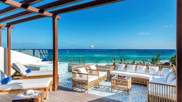 Ein überdachter Außenbereich mit Liegestühlen und Sofas, mit Blick auf einen Strand und den Ozean.