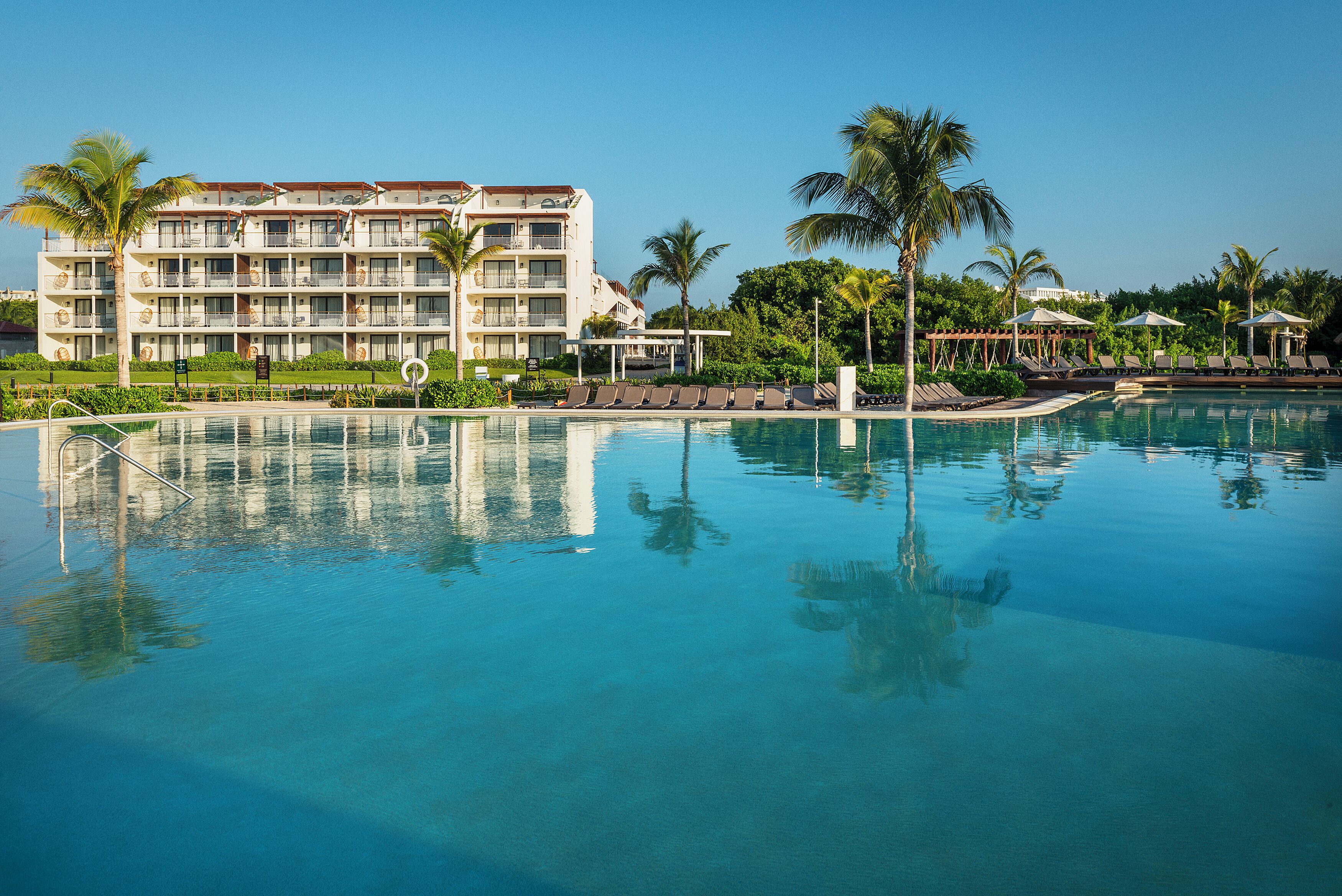 A hotel with a pool, palm trees, and lounge chairs.