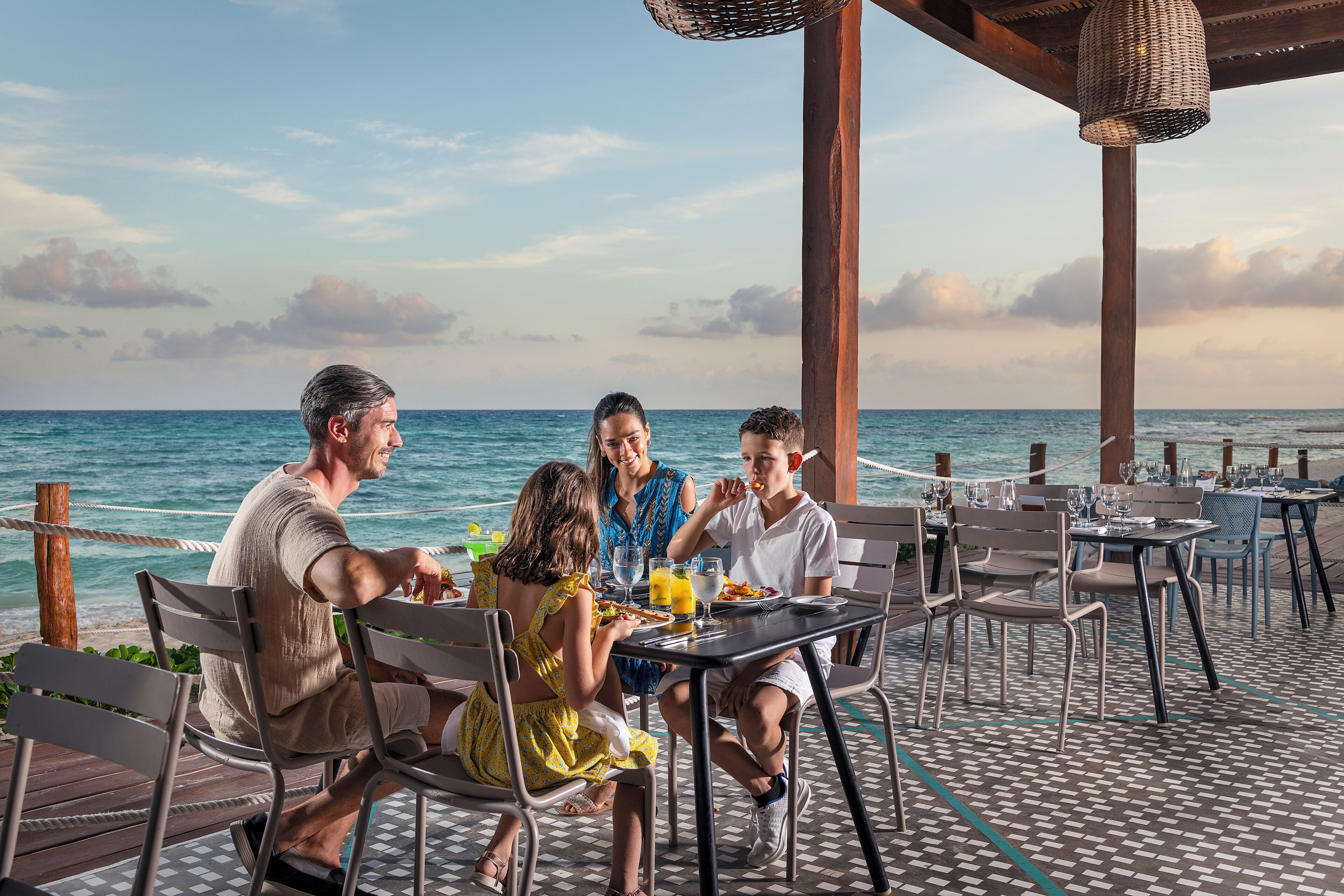 A group of people dining at an outdoor table with a view of the ocean.