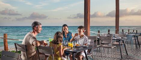 A group of people dining at an outdoor table with a view of the ocean.