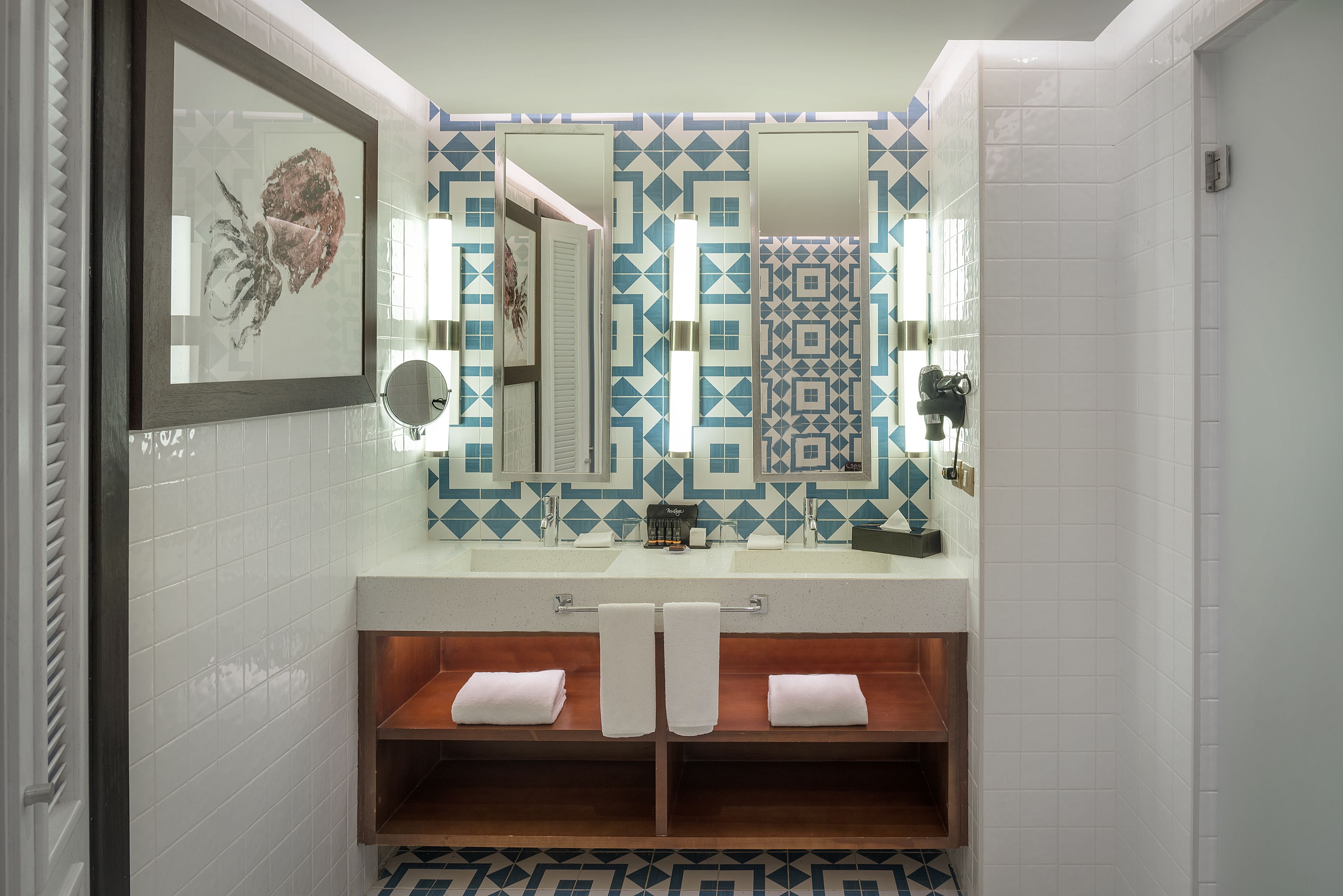 A bathroom with a white sink, two towel racks, a mirror, and a patterned tile backsplash.