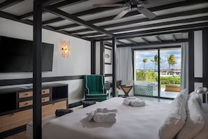 A hotel room with a bed, a TV, a green chair, a balcony with a view of palm trees and a pool.