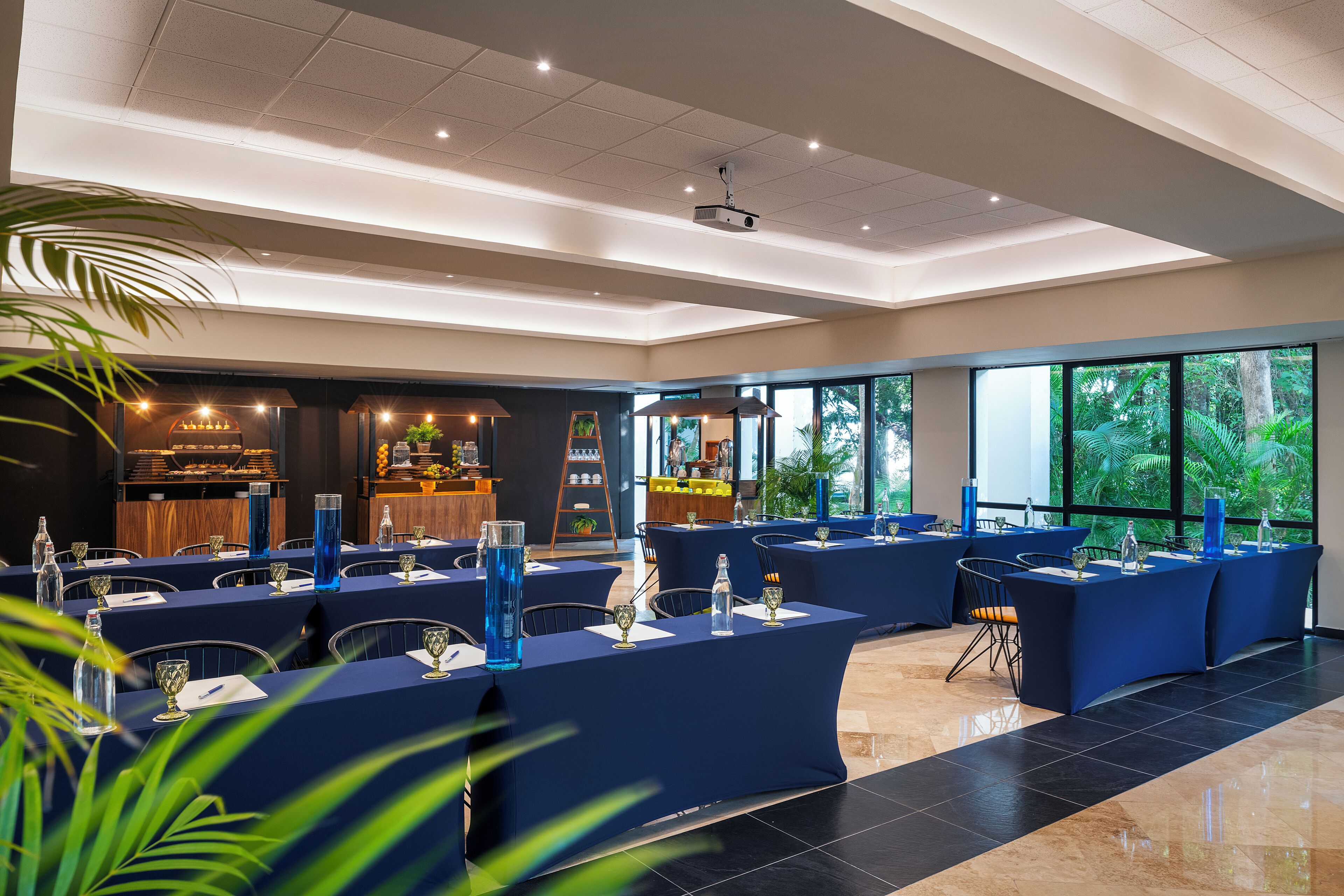 Une salle de conférence avec des tables disposées pour une réunion, de grandes fenêtres et un projecteur fixé au plafond.