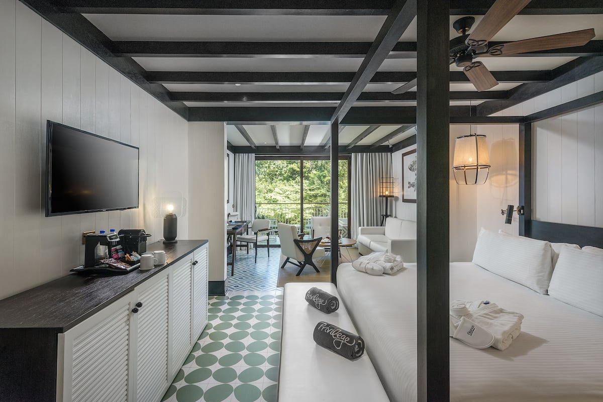 Una camera d'albergo con un letto grande, un divano, una TV e un'area pranzo con vista sul verde.