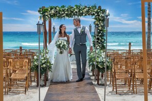 A wedding ceremony on a beach with a wooden aisle, chairs, and floral decorations. - Ocean Riviera Paradise All Inclusive (Playa del Carmen)