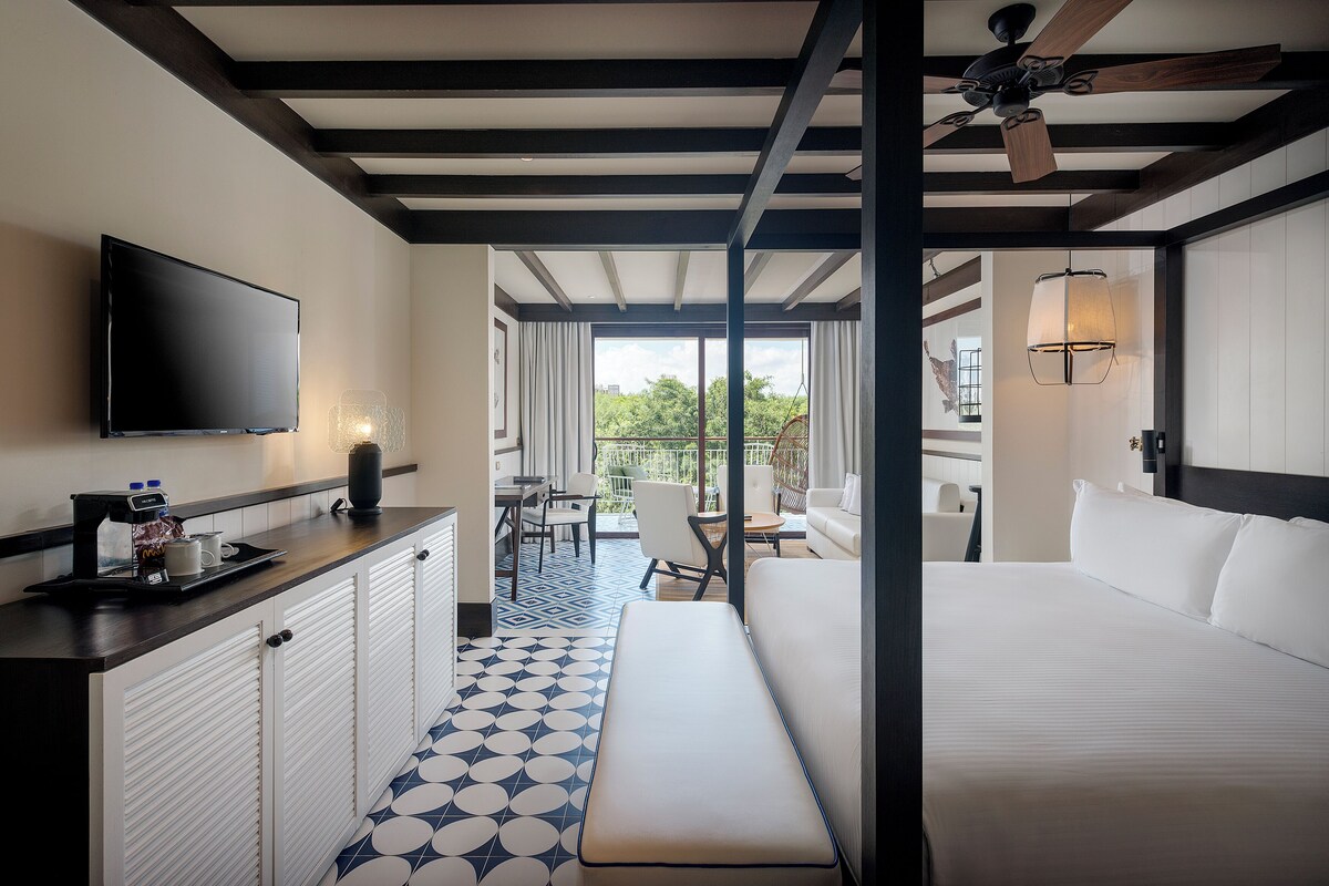 A hotel room with a bed, a TV, a coffee station, a balcony, and a ceiling fan.