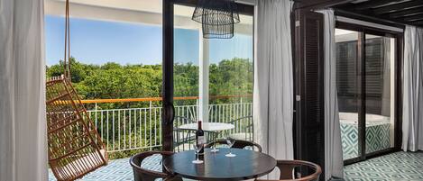 A balcony with a table and chairs, a hanging chair, and a view of greenery.