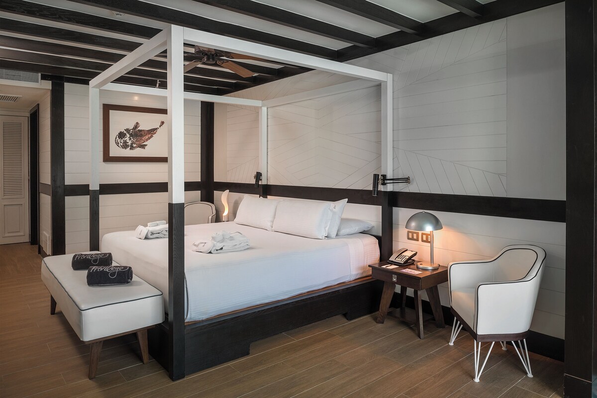 A four-poster bed with a white canopy, a bedside table with a lamp, and a chair.