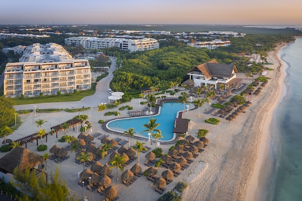A resort with a large pool, beachside lounge chairs, and a view of the ocean.