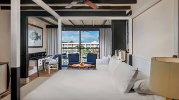 Une chambre d’hôtel avec un lit, un bureau, deux chaises, une table avec des fruits et un balcon avec vue.