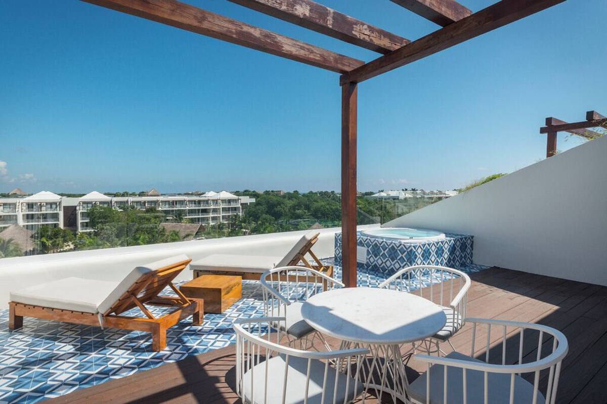 A rooftop terrace with lounge chairs, a table, and a hot tub.