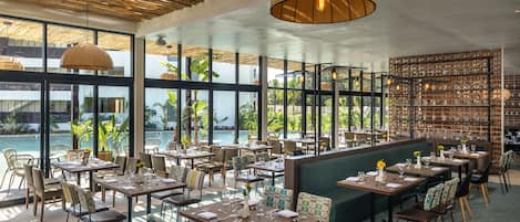 Restaurante com mesas e cadeiras dispostas para refeições, grandes janelas oferecendo vistas do exterior e teto com design trançado.