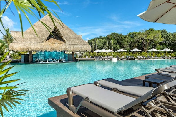 A pool area with lounge chairs, a bar, and a thatched-roof structure. - El Beso Adults Only at Ocean Riviera Paradise - All Inclusive (Playa del Carmen)