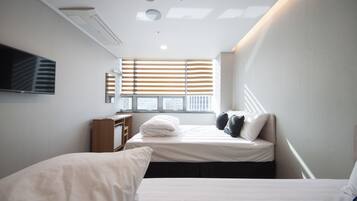 Una habitación de hotel moderna con un ventanal grande, un televisor de pantalla plana en la pared y dos camas con ropa blanca.
