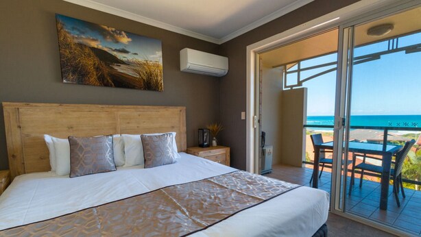 Une chambre avec un grand lit, un tableau au-dessus du lit, un climatiseur fixé au mur et un balcon avec une table et des chaises.