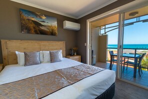 Un dormitorio con una cama grande, un cuadro sobre la cama, un aire acondicionado en la pared y un balcón con una mesa y sillas.