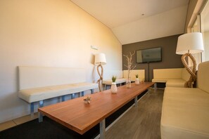 A modern living room with a wooden coffee table, white sofas, and a flat-screen TV mounted on the wall. - Beach Haven Executive Apartments (Korora)