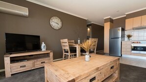 Un salon moderne doté d’un téléviseur à écran plat, de meubles en bois, d’une horloge et d’un coin cuisine.