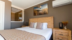Une chambre avec un grand lit, une tête de lit en bois, une table de chevet avec des tiroirs, un miroir et un appareil de climatisation fixé au mur.