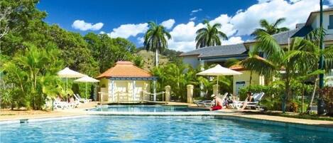 Una piscina al aire libre, sombrillas, sillones reclinables de piscina