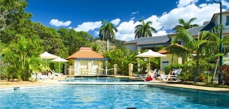 Una piscina al aire libre, sombrillas, sillones reclinables de piscina