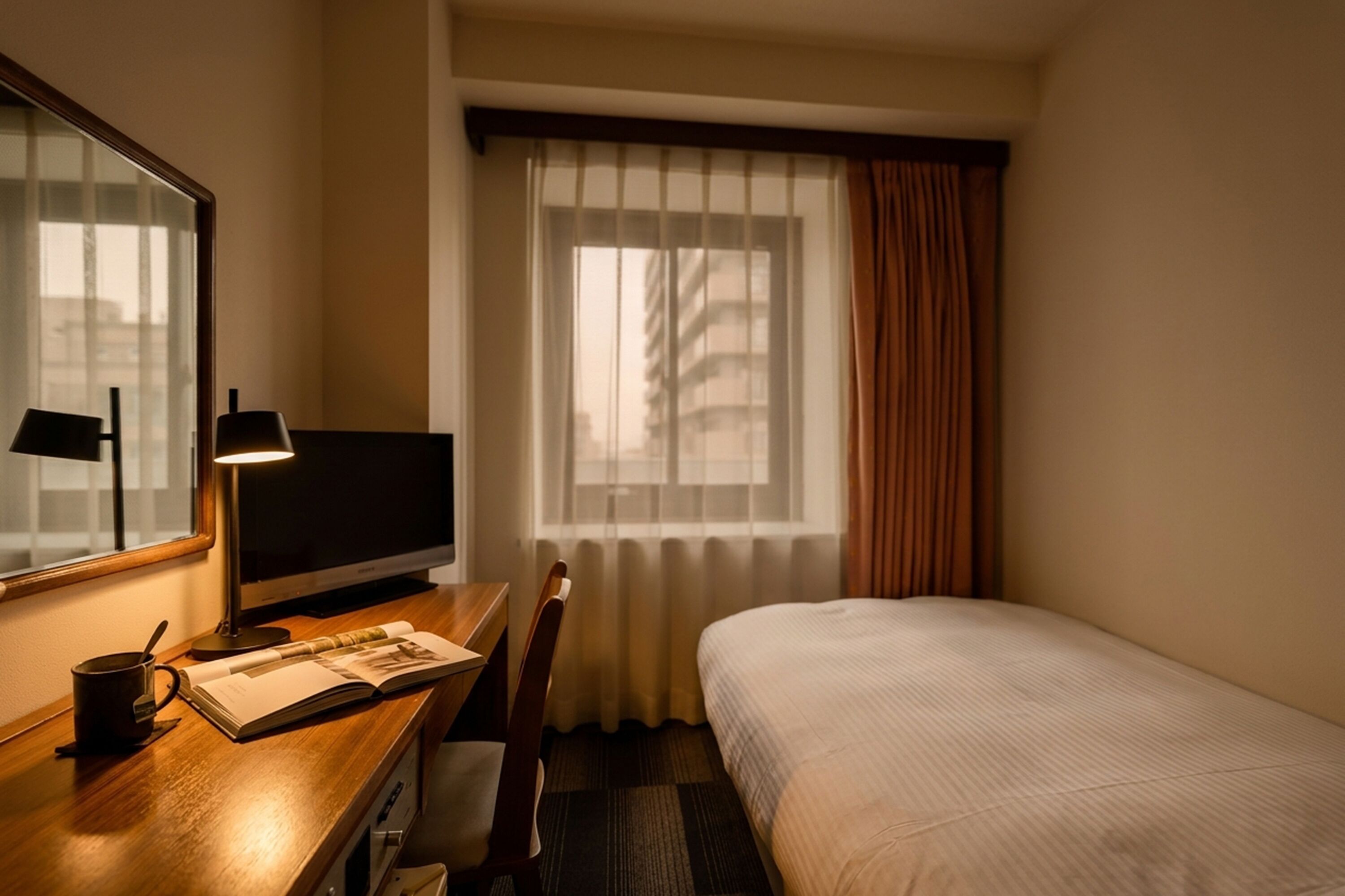 Hotelkamer met een bed, een bureau met lamp, een stoel, een televisie en een raam met gordijnen.