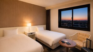 A hotel room with two beds, a desk, a chair, a table, and a window with a city view. - City Hotel Airport in Prince (Izumisano)