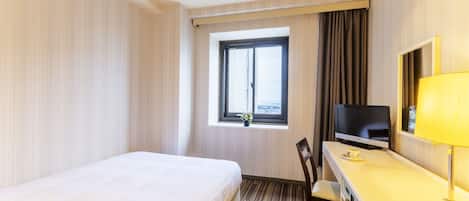 A hotel room with a bed, a desk with a television, a chair, and a window with curtains.