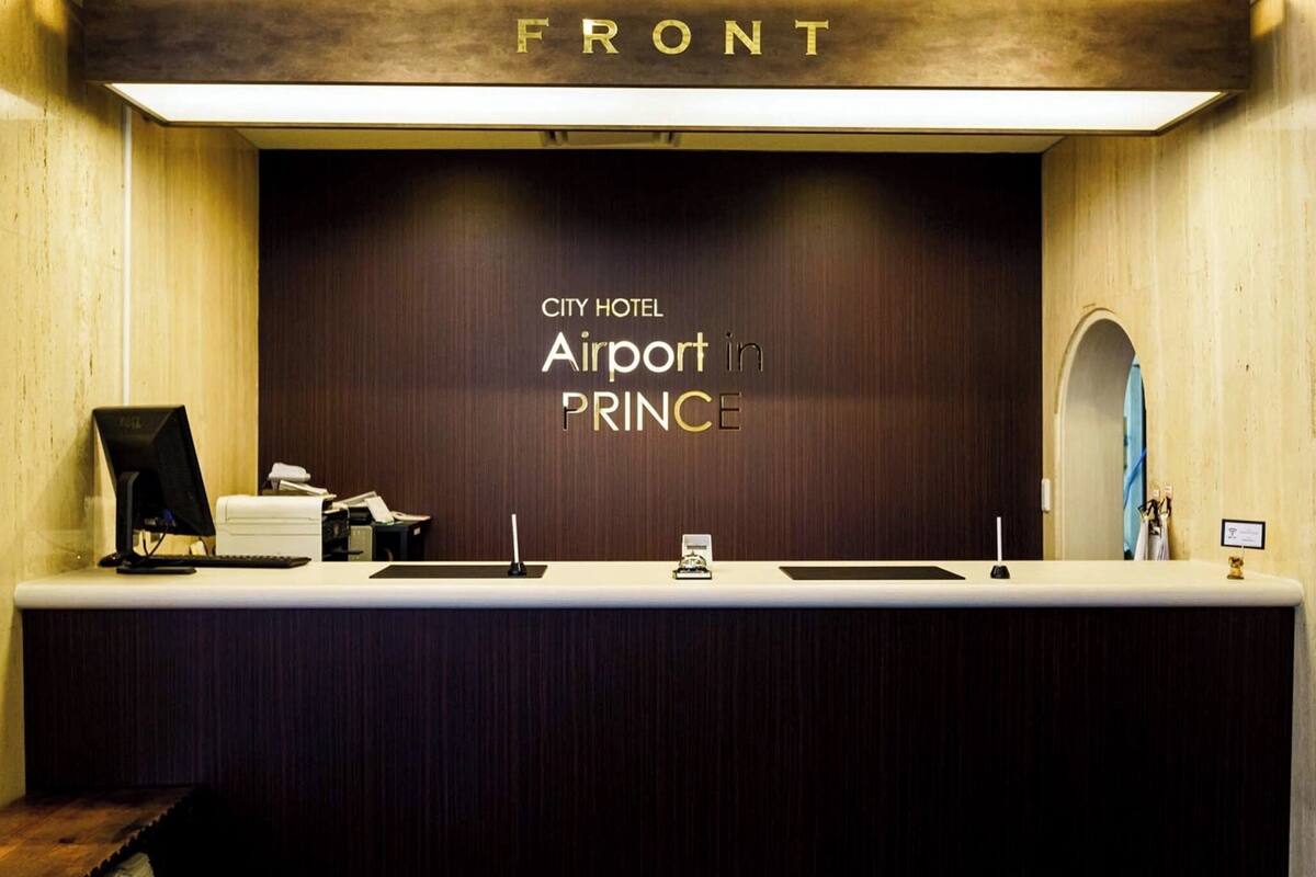 A reception desk at City Hotel Airport in PRINCE with a wooden front panel and a sign above it.