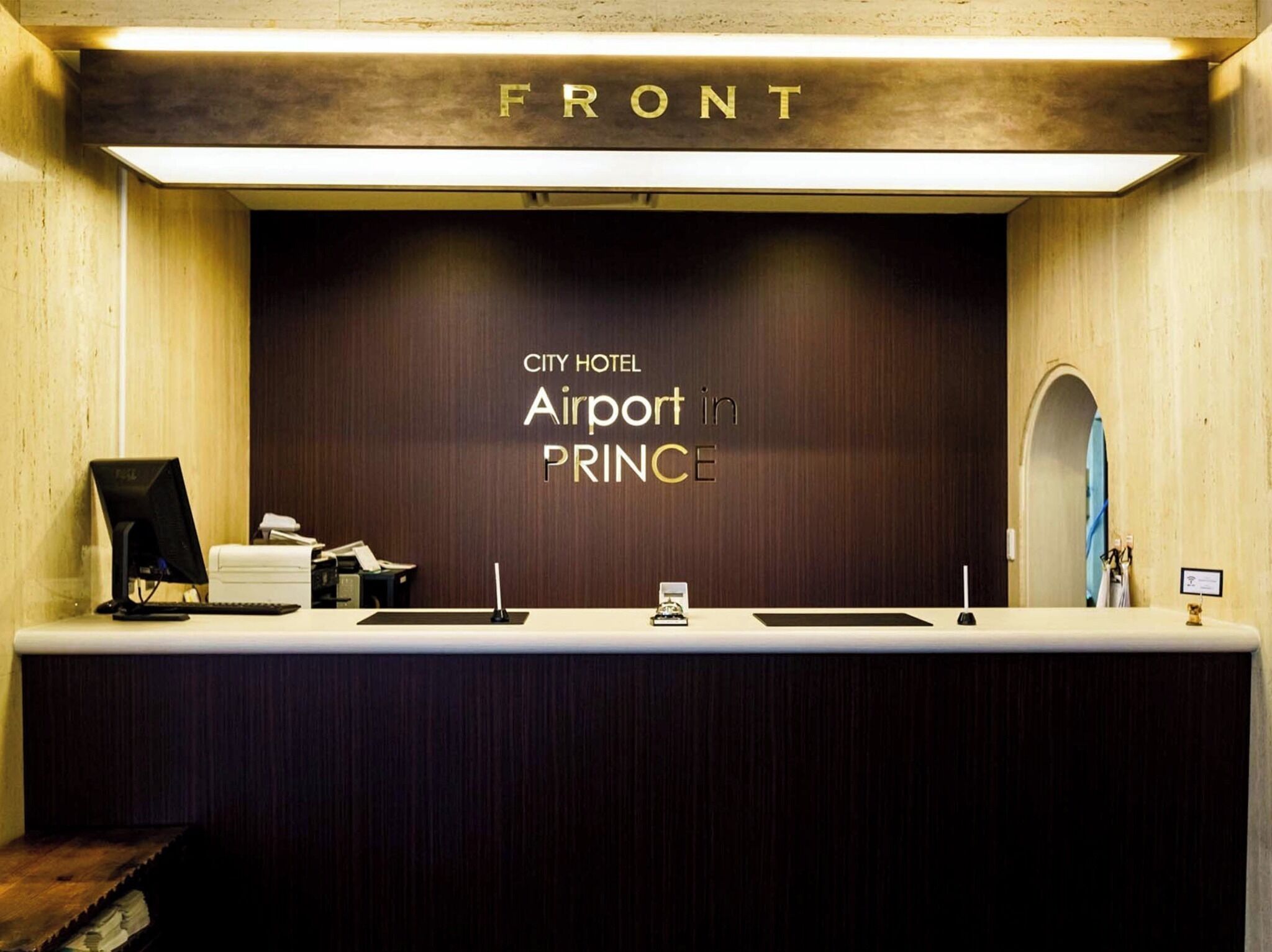 A reception desk at City Hotel Airport in PRINCE with a wooden front panel and a sign above it.