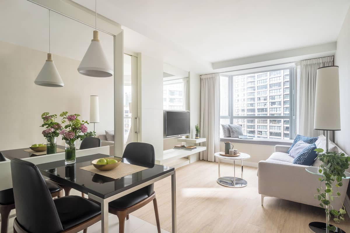 A modern living room with a dining area, a sofa, a TV, and a large window with a city view.