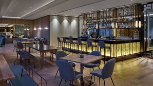 Eine moderne Bar mit einer Marmorplatte und einer Auswahl an Spirituosenflaschen. Mehrere Tische und Stühle sind zum Essen oder für die Geselligkeit angeordnet.